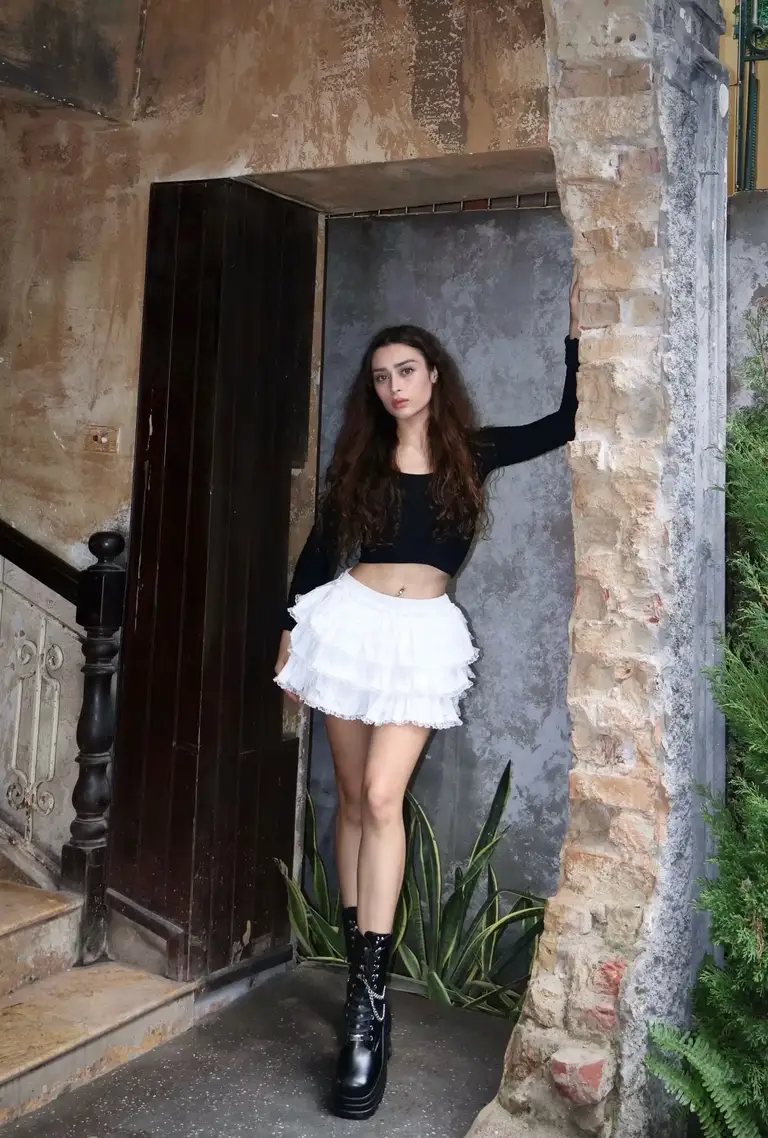 Trong ảnh, người đẹp kết hợp áo crop top đen, chân váy xếp tầng trắng và boots cao cổ, tạo tổng thể vừa cá tính, thời thượng vừa vẫn giữ được nét nữ tính