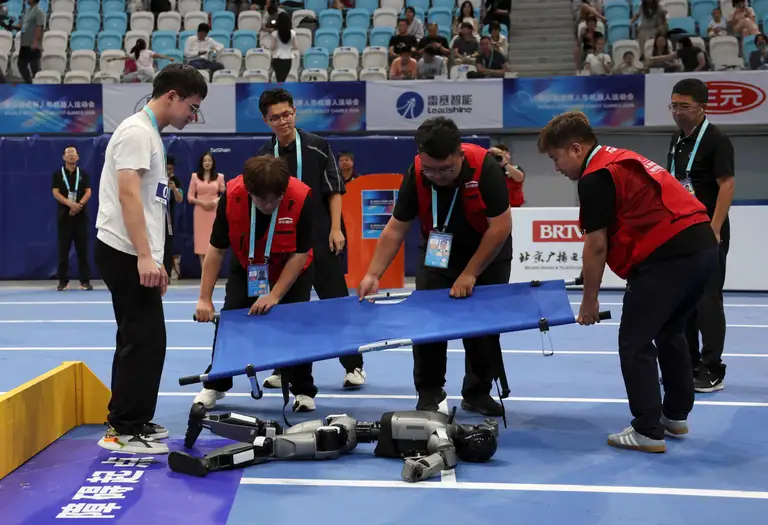 Các nhân viên mang cáng để di chuyển một robot hình người "gục ngã" sau khi không thể hoàn thành bài thi chạy 400m vượt chướng ngại vật trong khuôn khổ Thế vận hội Robot hình người tại Bắc Kinh (Trung Quốc) - Ảnh: REUTERS