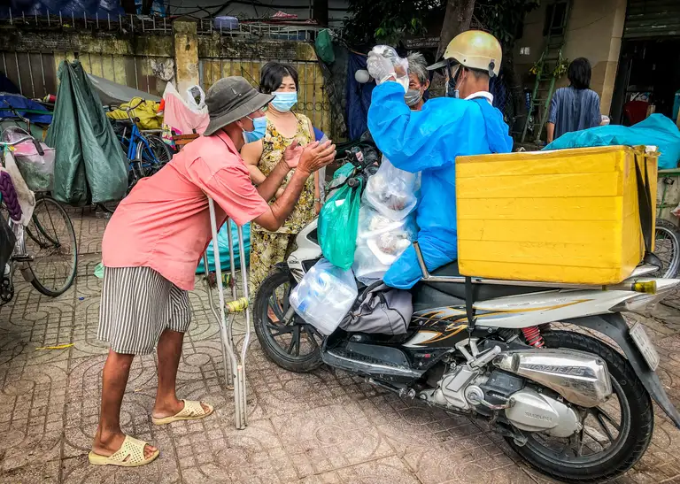 Giữa trưa tháng 8-2021, trời đang nắng gắt nhưng vì lo cho người dân tới giờ cơm, ông Tạ Anh Dũng (ở quận 8 cũ, là võ sư) dù đã bị cụt một chân nhưng mặc lên mình bộ đồ bảo hộ và xếp đầy các phần cơm lên xe rồi chạy vội đi đến từng con đường, ngõ hẻm để trao tận tay từng người - Ảnh: CHÂU TUẤN