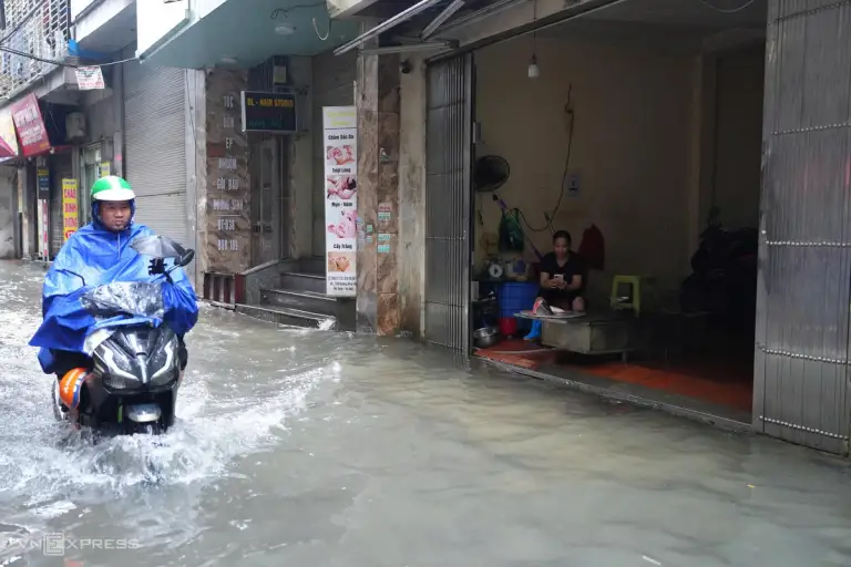 Người phụ nữ bình thản ngồi xem điện thoại trước cửa nhà, trong khi ngoài đường Phú Mỹ ngập sâu gần hết bánh xe máy. Ảnh: Văn Ngọc