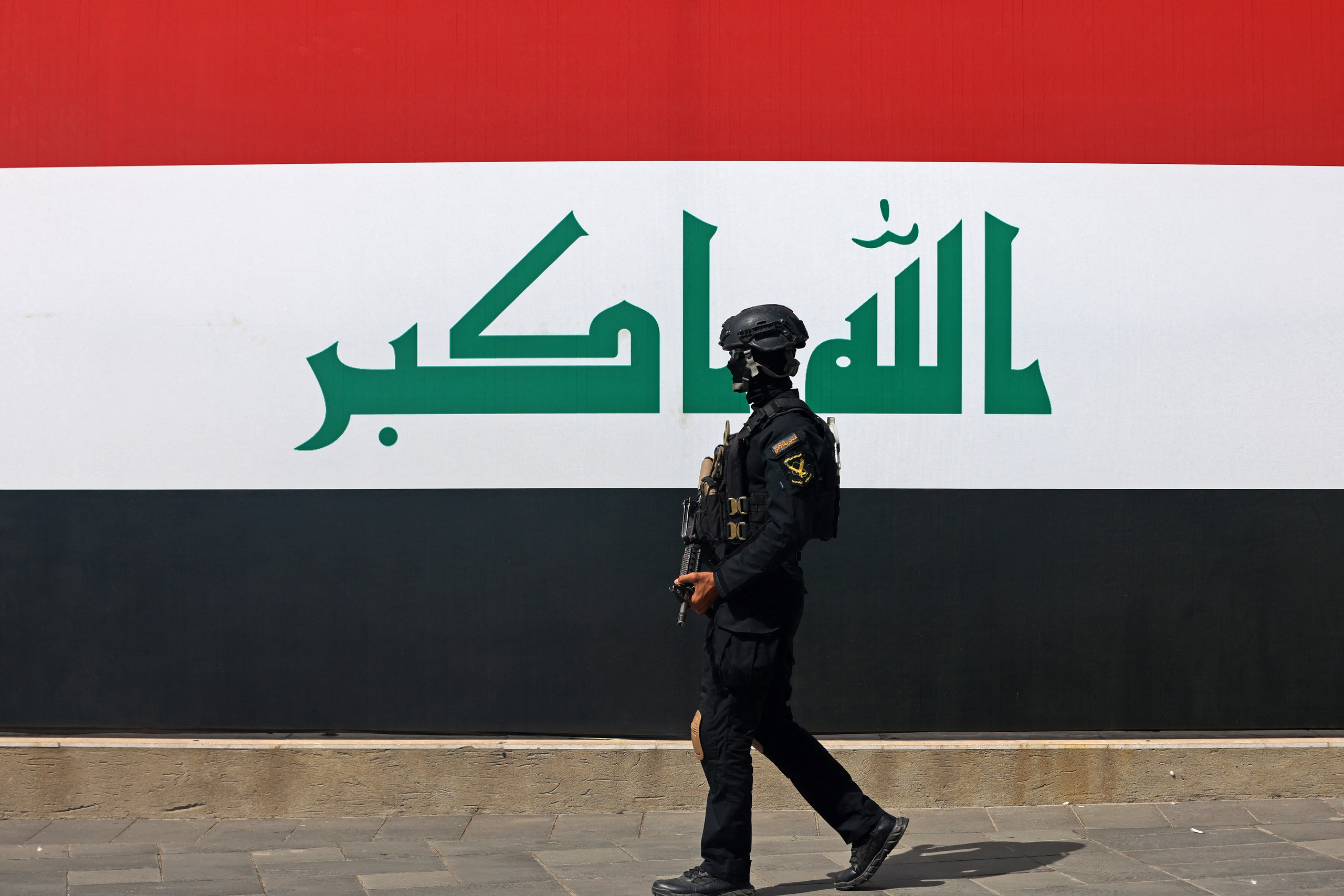 Một thành viên lực lượng an ninh Iraq đi ngang quốc kỳ khổng lồ tại quảng trường Tahrir ở Baghdad ngày 29-9, trước thời điểm liên quân do Mỹ dẫn đầu kết thúc sứ mệnh tại nước này - Ảnh: AFP