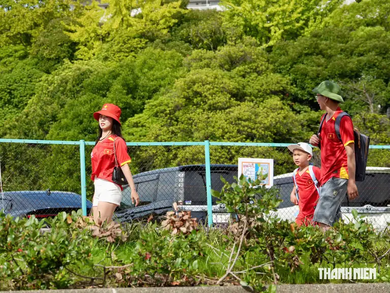 Một gia đình nhỏ với 2 vợ chồng và con nhỏ đi bộ vào sân Nagoya City Minato Soccer Field, với bộ đồng phục áo đội tuyển Việt Nam rực rỡ